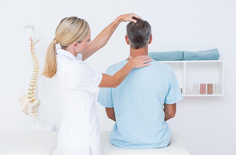 Una doctora examina el cuello y la zona cervical de un paciente que está de espaldas.